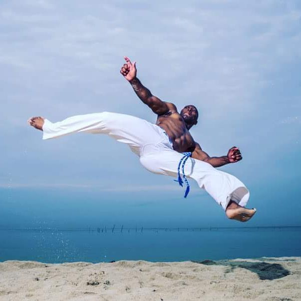 A man in white pants is jumping in the air on a beach.