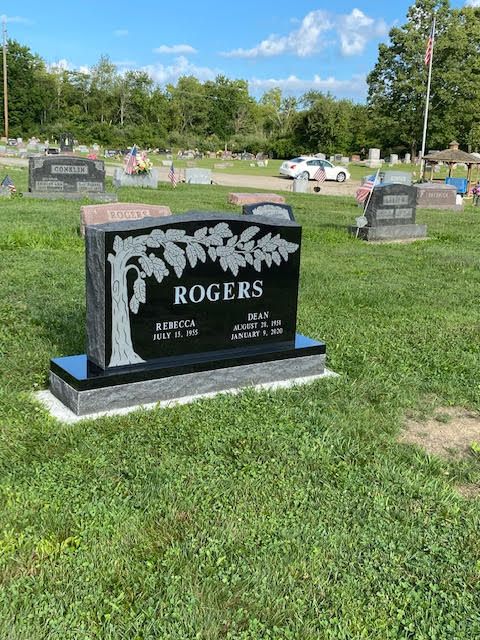 A black gravestone with a tree on it is in a cemetery.