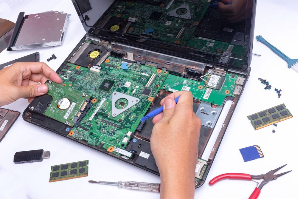 A person is repairing a laptop computer with a screwdriver.