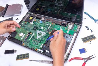 A person is repairing a laptop computer with a screwdriver.