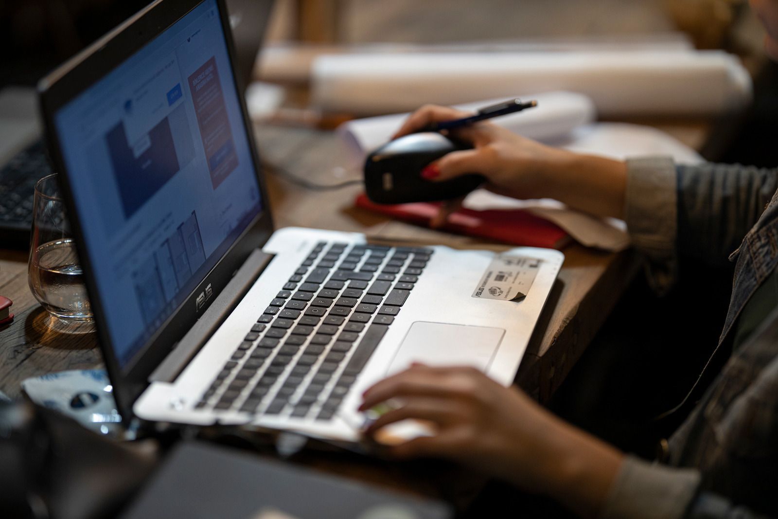 A person is typing on a laptop while holding a pen