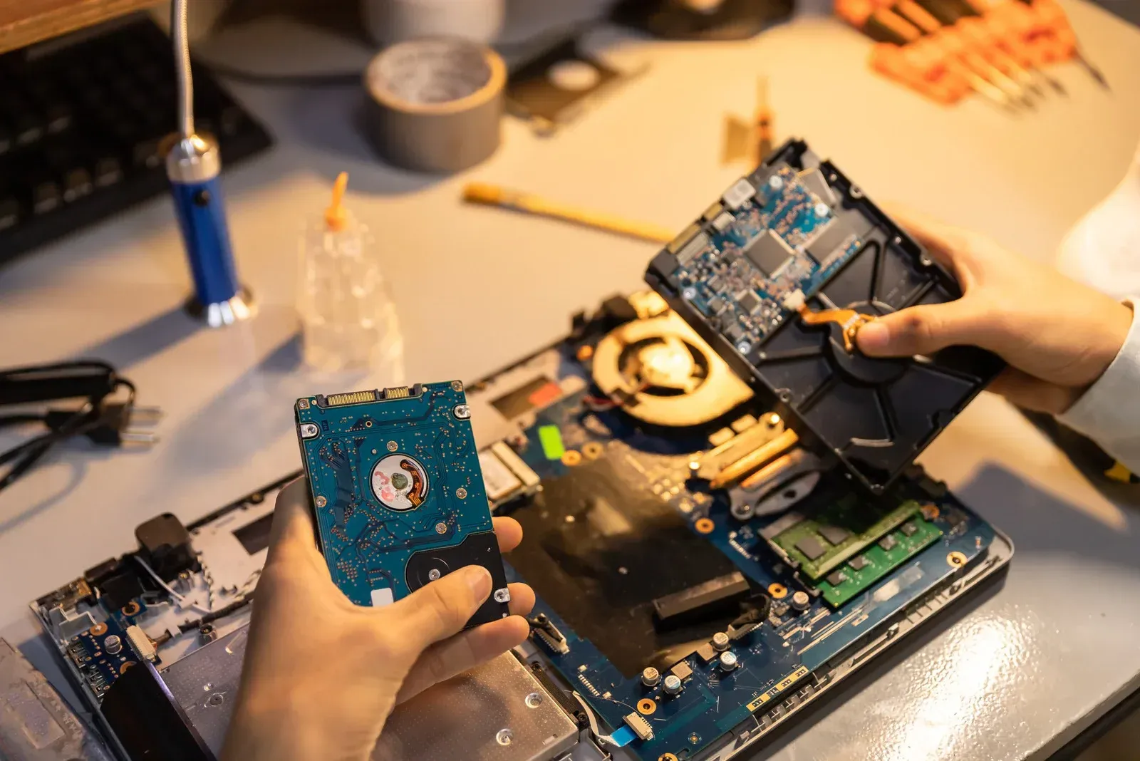 A person is holding a hard drive in front of a laptop computer.