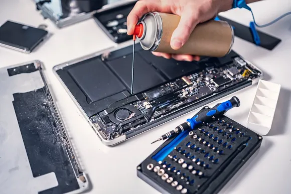 A person is cleaning a laptop with a spray bottle.