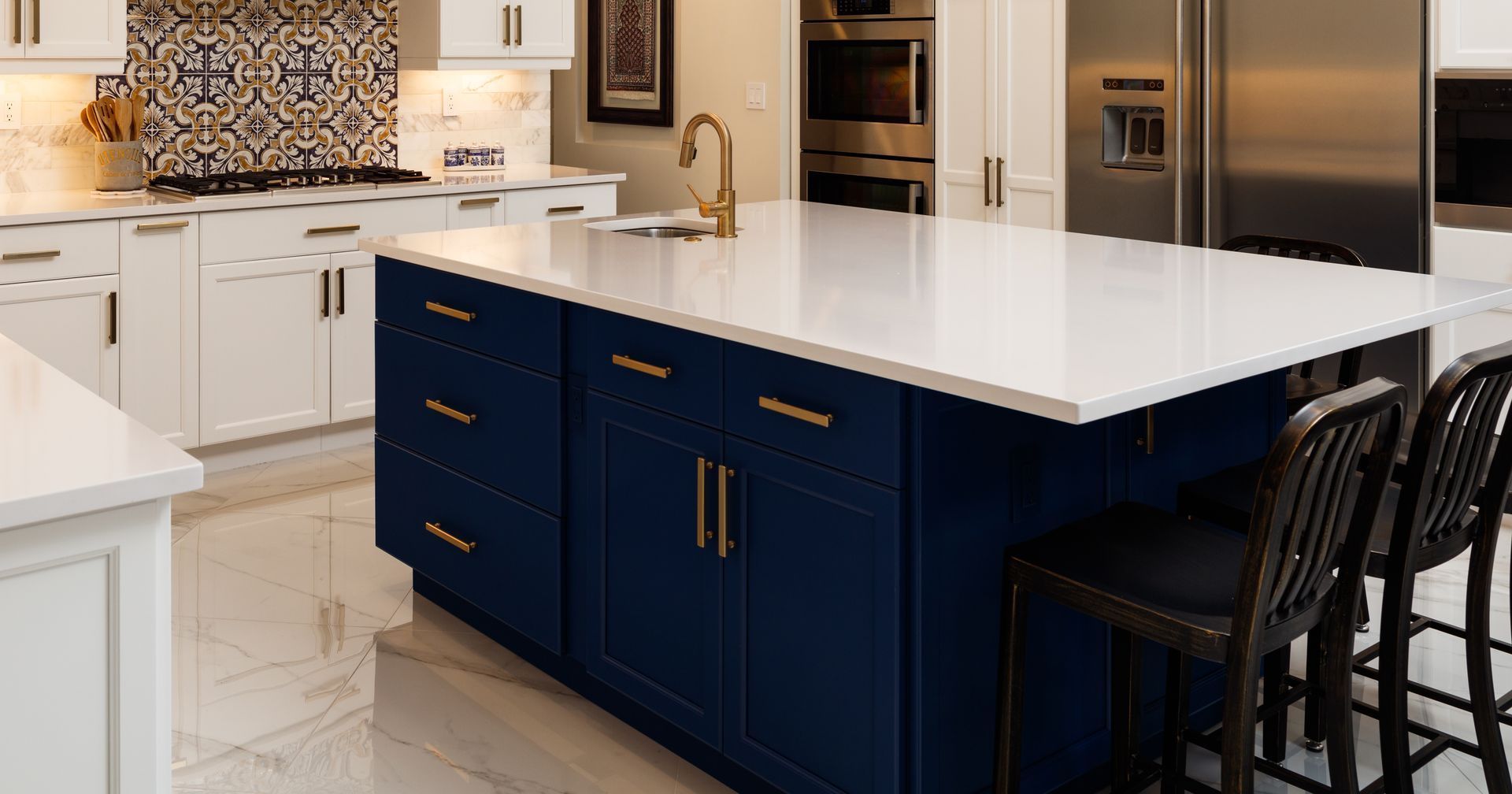 Cuisine avec îlot bleu, comptoirs blancs, quincaillerie dorée et deux tabourets.