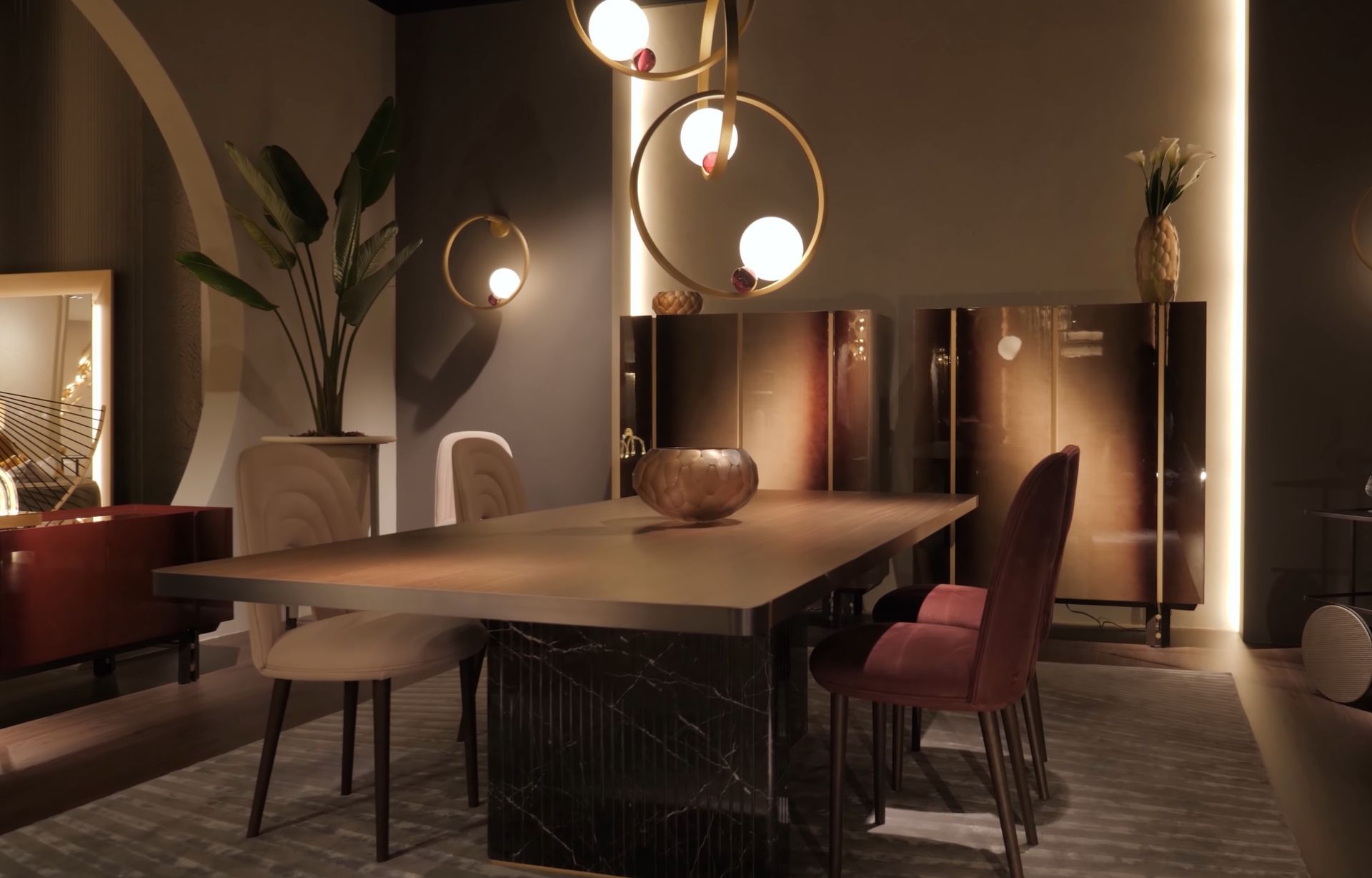 Salle à manger avec table, chaises, luminaires dorés, buffet et plantes décoratives.