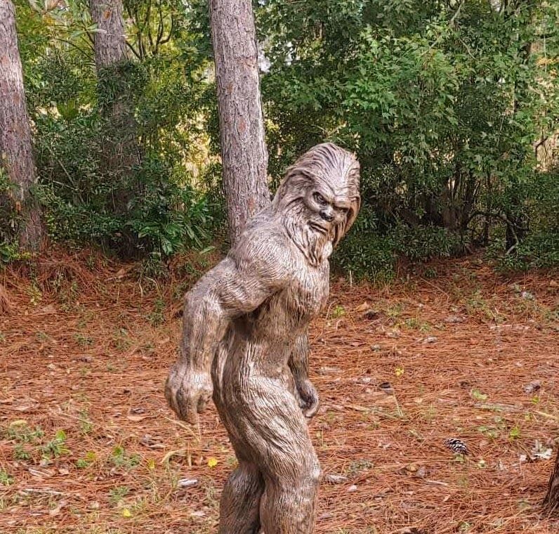 A wooden statue of a bigfoot is standing in the woods.