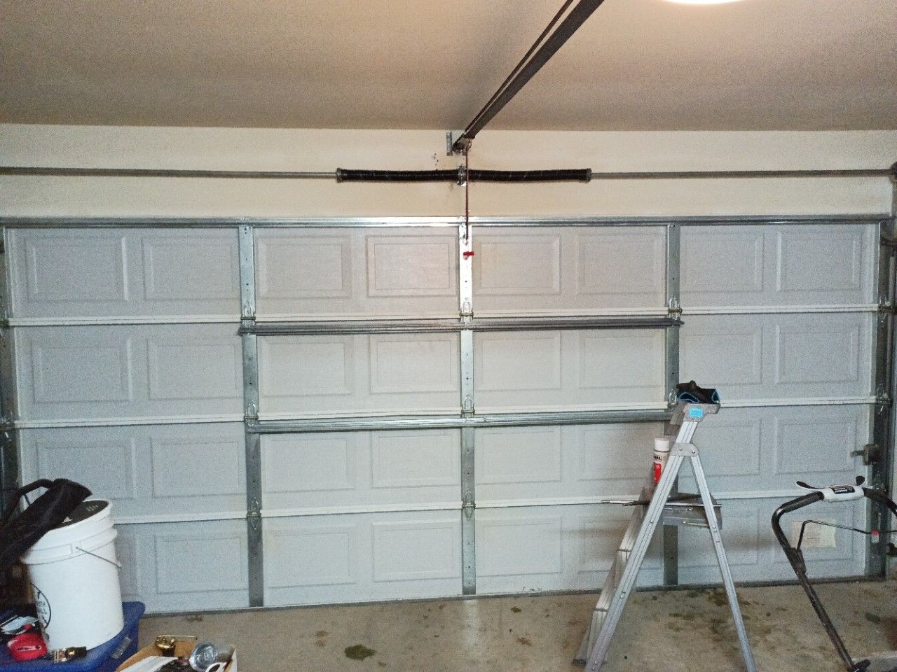 White closed garage door with metal frame; ladder and tools are present.