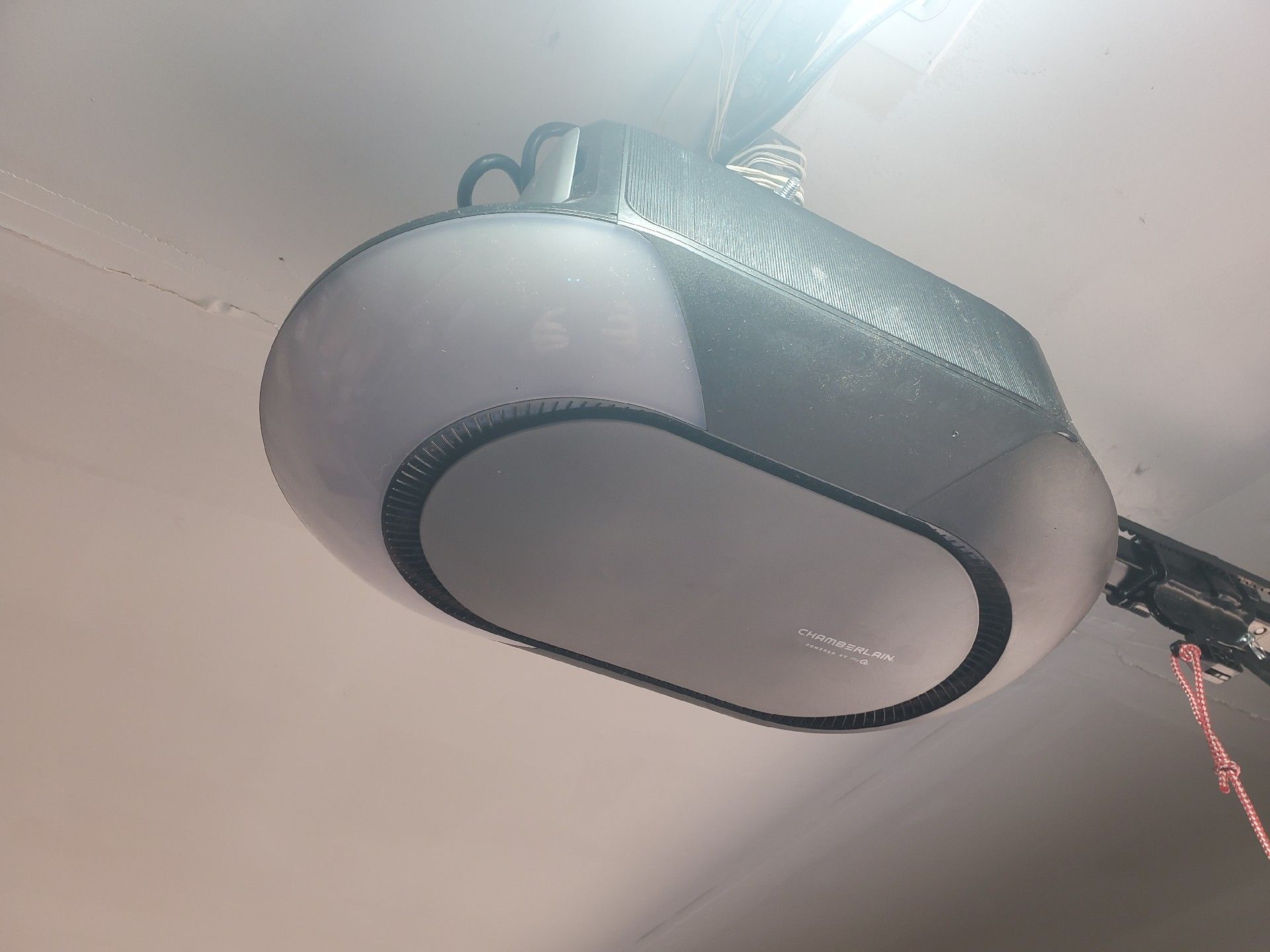 Garage door opener mounted on a ceiling, with a white and gray rounded housing, wires, and a light.