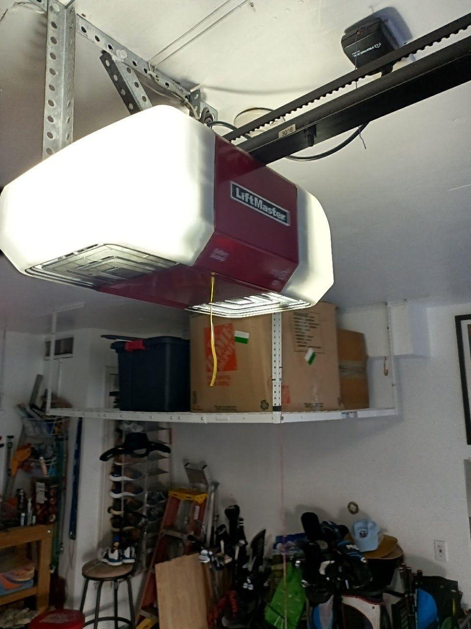 Garage door opener in a cluttered garage, with boxes on a shelf.