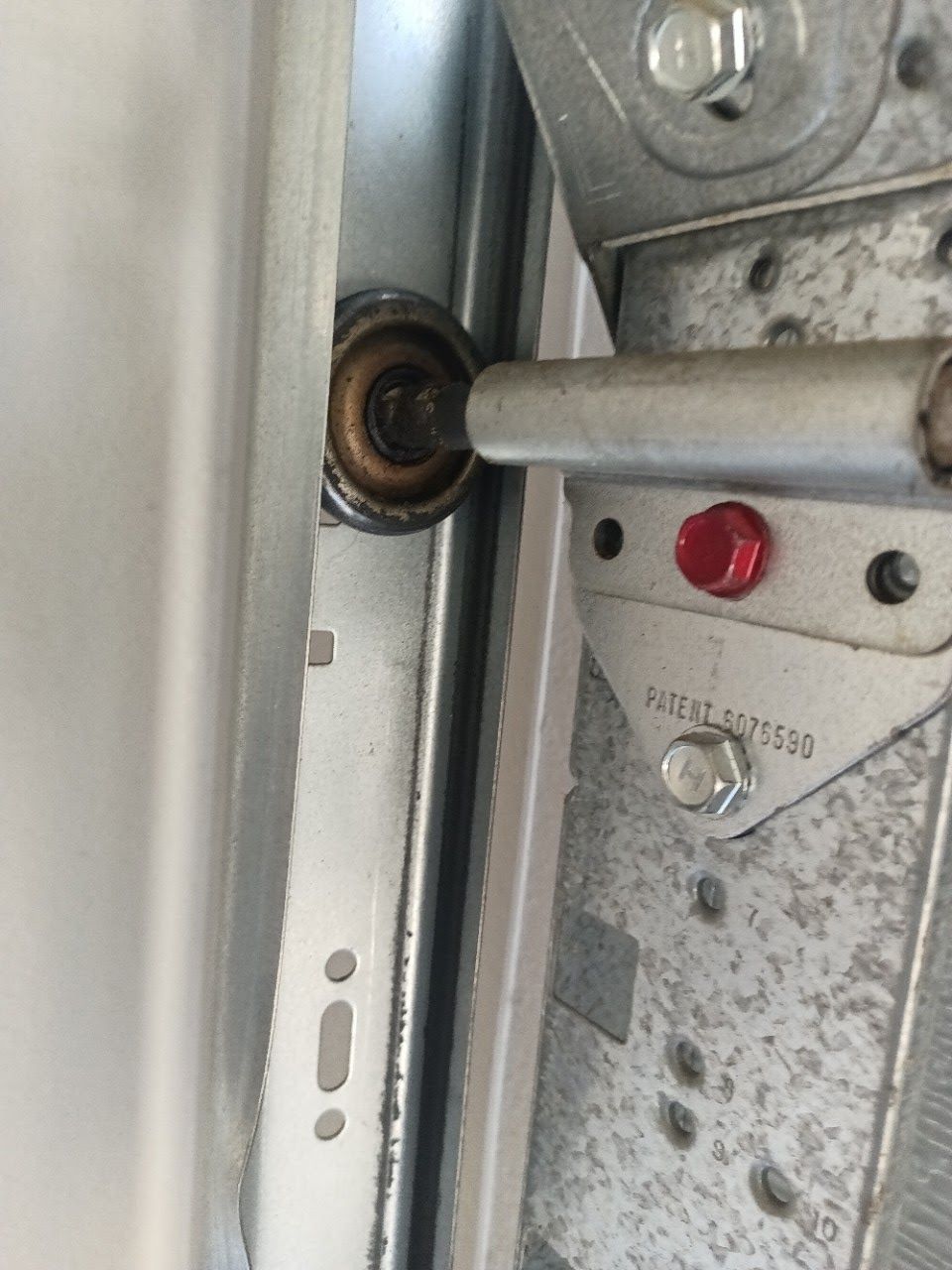 Garage door roller and track, close-up. Metal components with a rusty roller and a red bolt.