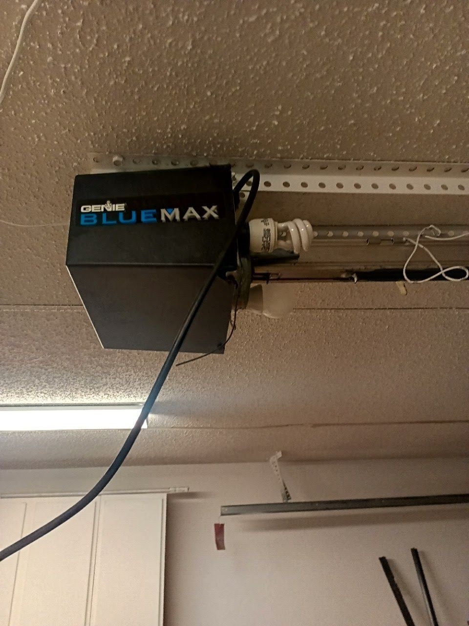 BlueMax garage door opener mounted on a garage ceiling with a black power cord.