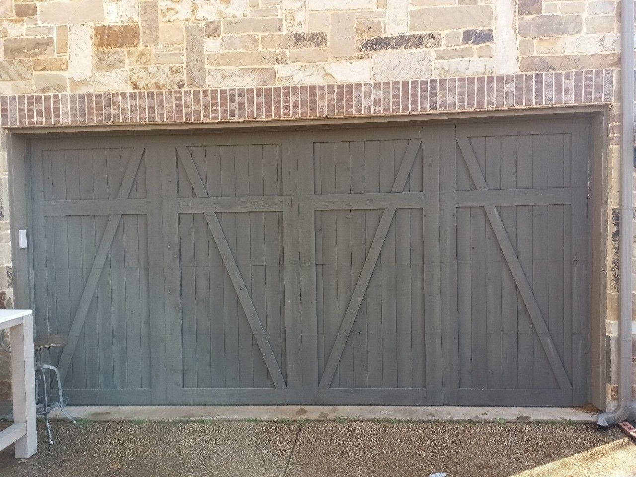 Gray wooden garage door with decorative diagonal braces, set against a stone brick wall.