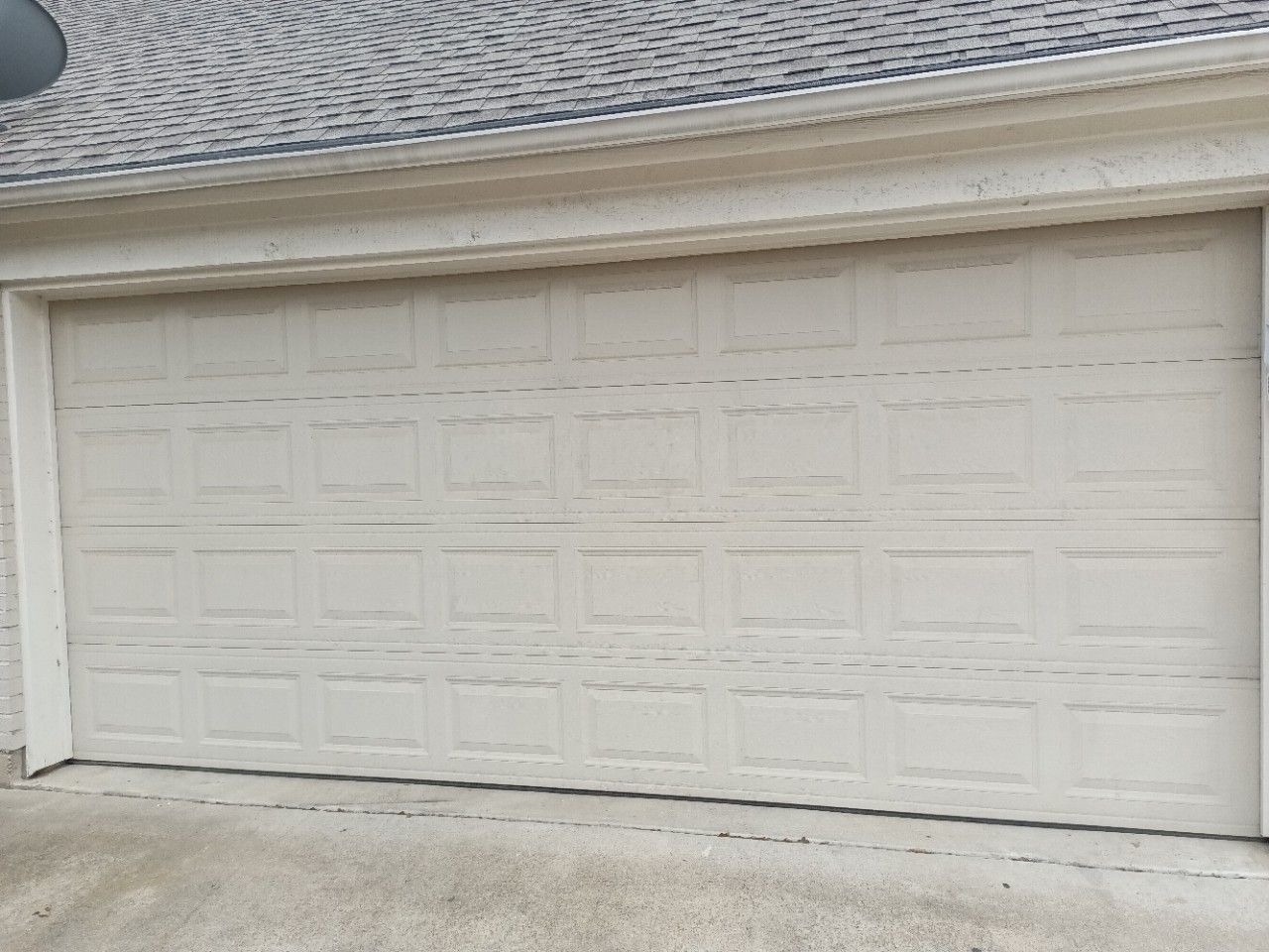 Closed, off-white garage door with rectangular panels, beneath a light gray roof.