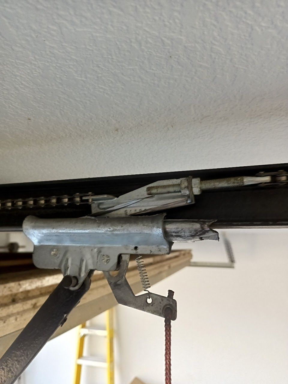 Garage door opener mechanism with chain, metal arms, and adjusting rod.