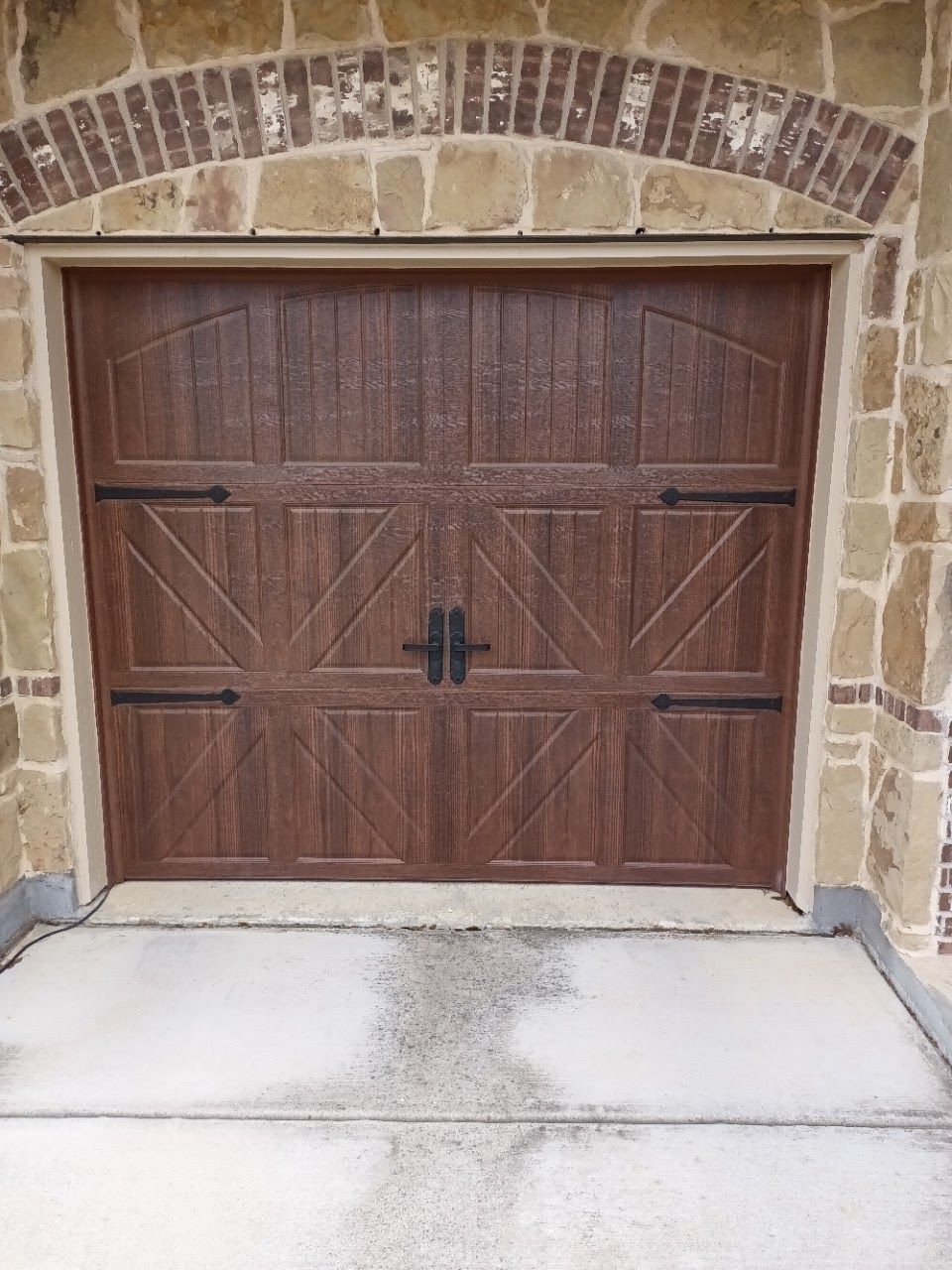 Brown wooden garage door with decorative hardware, set in a stone and brick archway.
