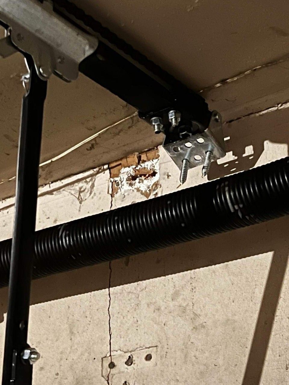 Garage door components attached to a ceiling, with damaged wood visible.