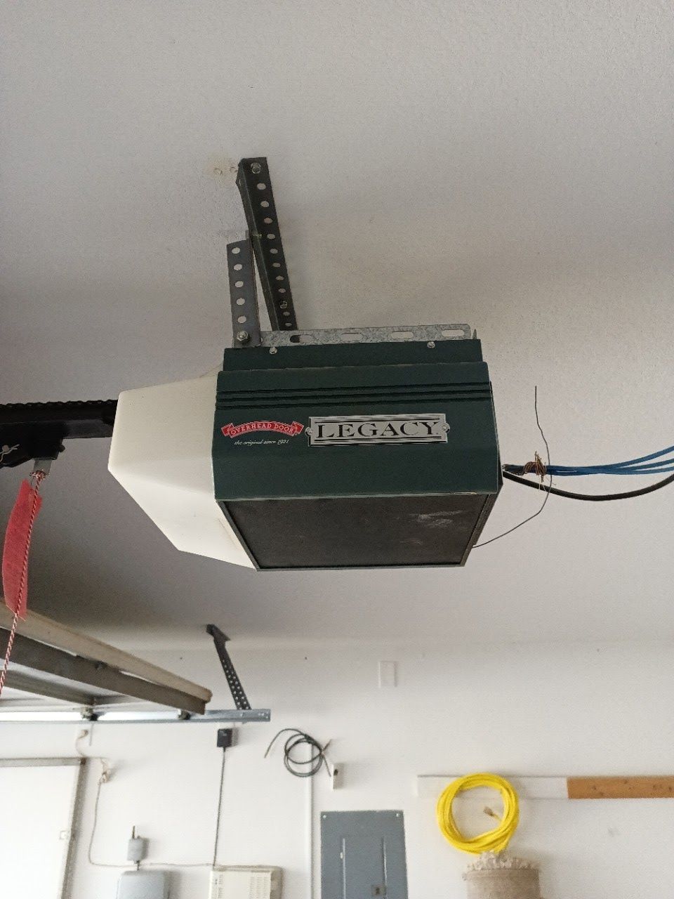 Garage door opener mounted on ceiling, with a black and green box and metal track.