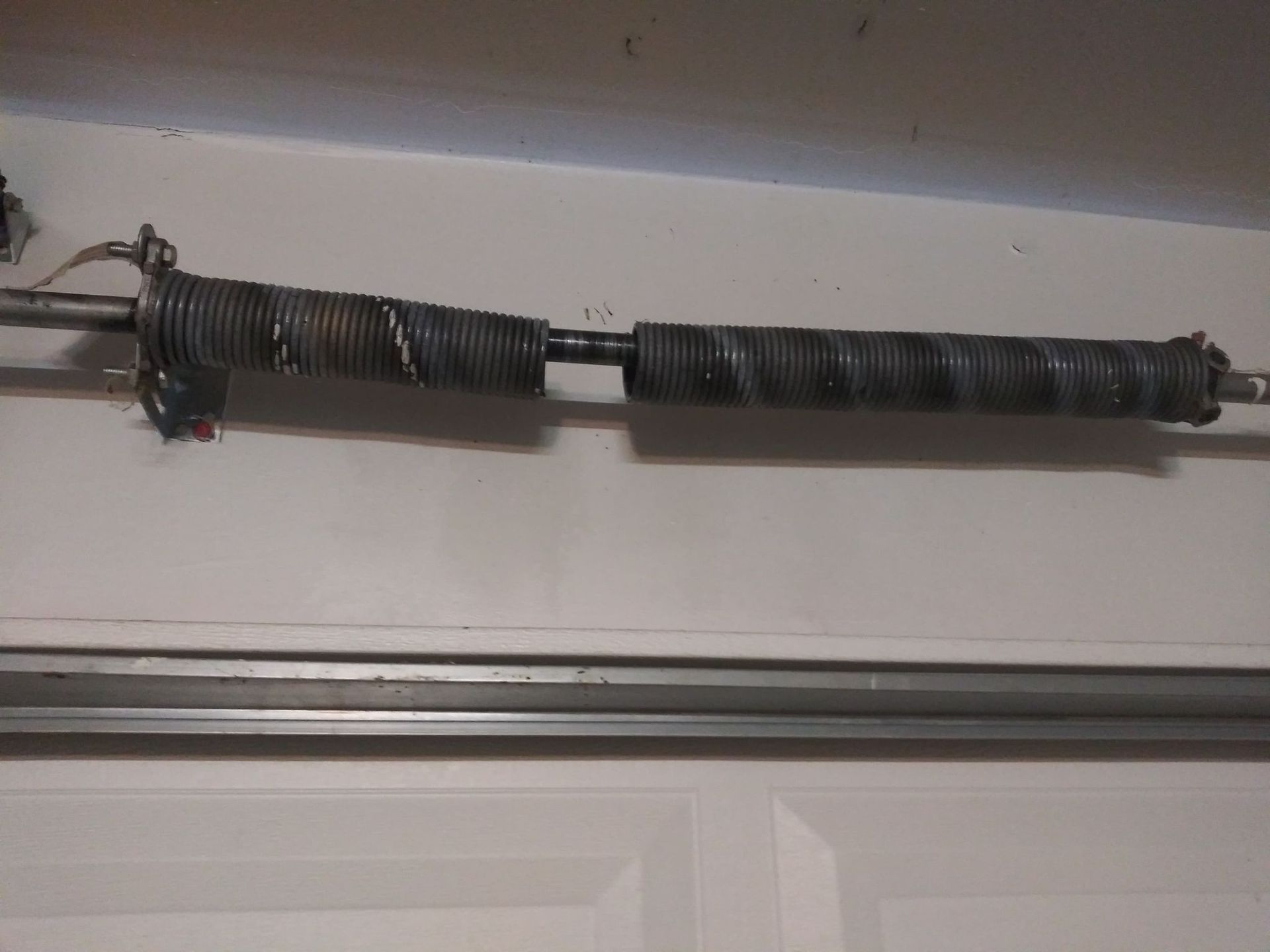 Broken garage door spring on a horizontal bar above a closed white garage door.