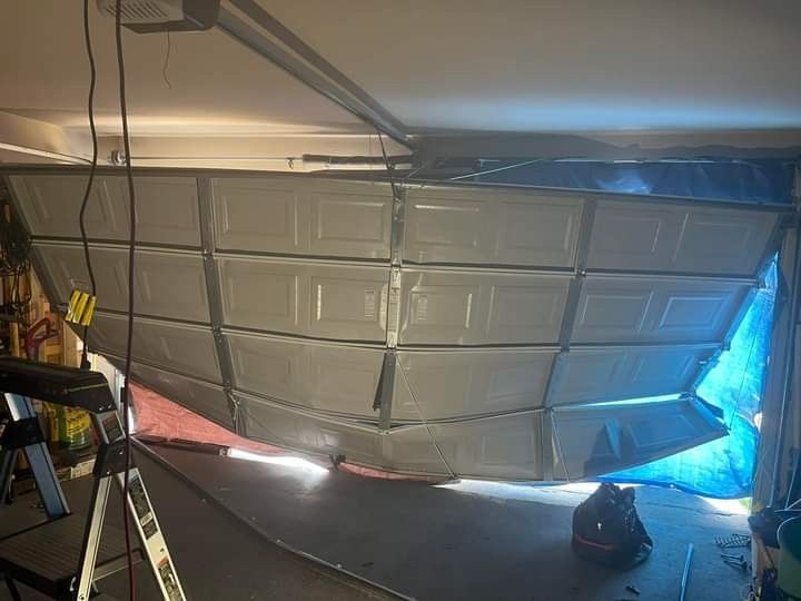 Damaged garage door, buckled inwards, likely from impact. Interior view, visible ceiling and open space behind.