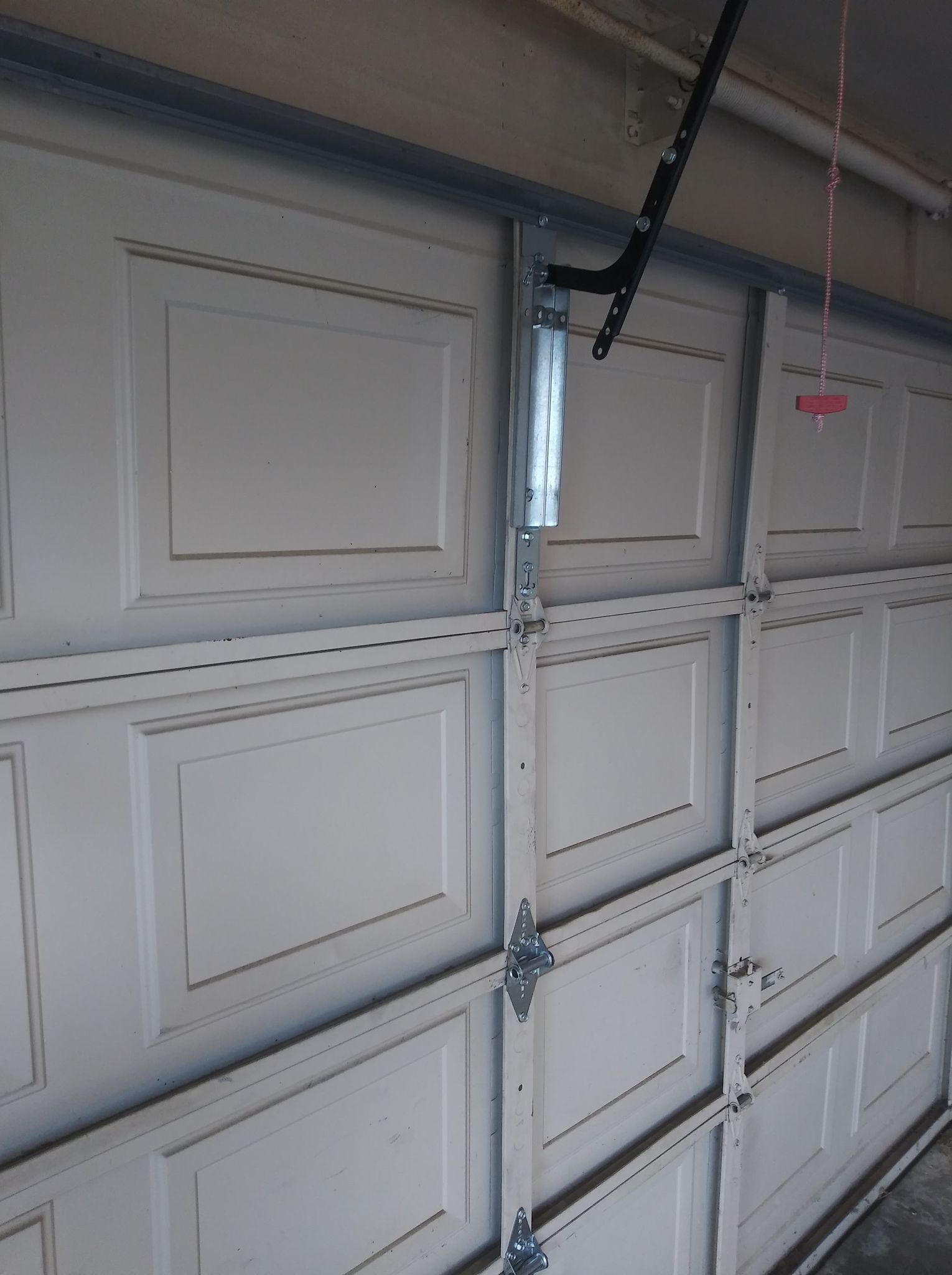 Garage door with white panels and metal tracks, partially open.
