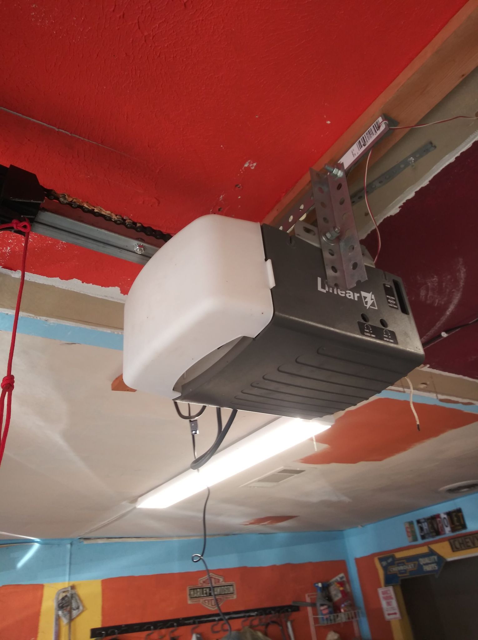 Garage door opener mounted on a red and white ceiling with a light fixture.