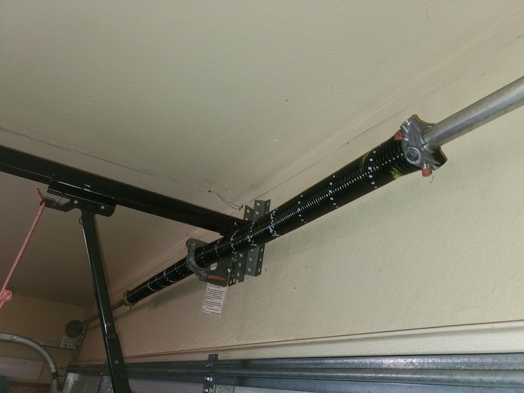 Garage door torsion spring assembly, black spring, mounted above door.