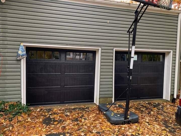 Two black garage doors with white trim, next to each other, surrounded by fall leaves and a basketball hoop.