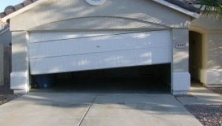 Garage door partially open, appearing misaligned, in front of a house.
