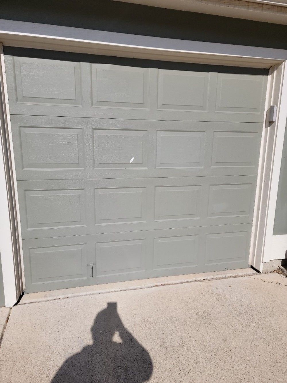 Gray garage door with panel design, casting shadow of a person holding a phone.