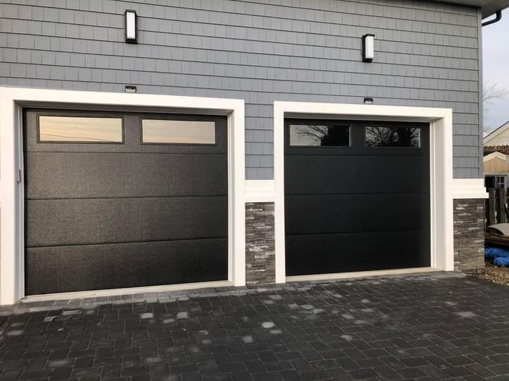 Two black garage doors with white trim, gray siding, and stone accents.