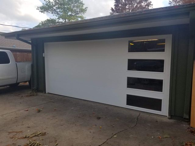 White garage door with rectangular windows, in front of a green garage. A light-colored pickup truck is partially visible to the left.