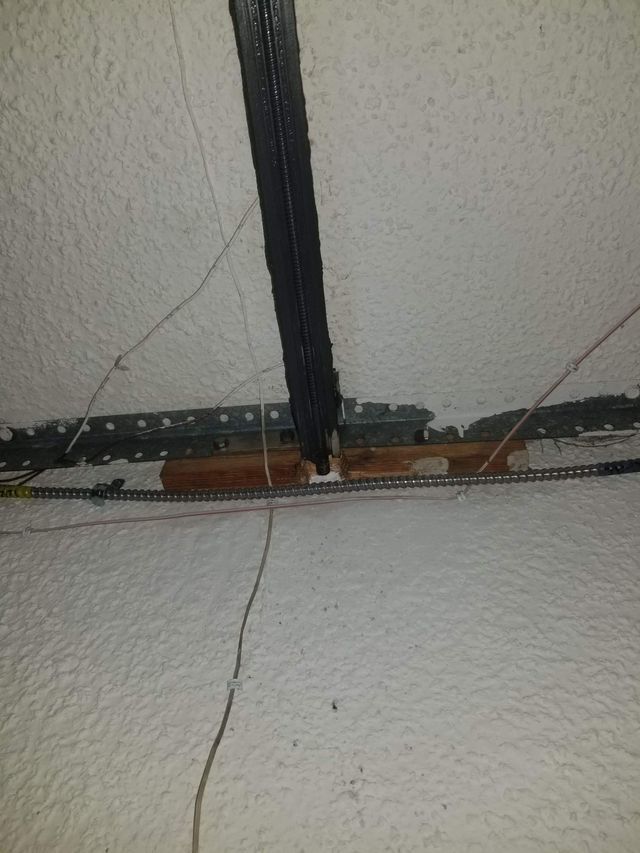 A garage door opener rail and chain attached to the ceiling. The ceiling is white with texture, and wires are visible.