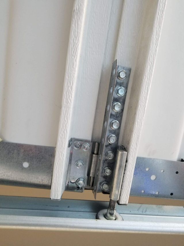 Garage door hinge assembly, with metal brackets and bolts, attached to a white panel.