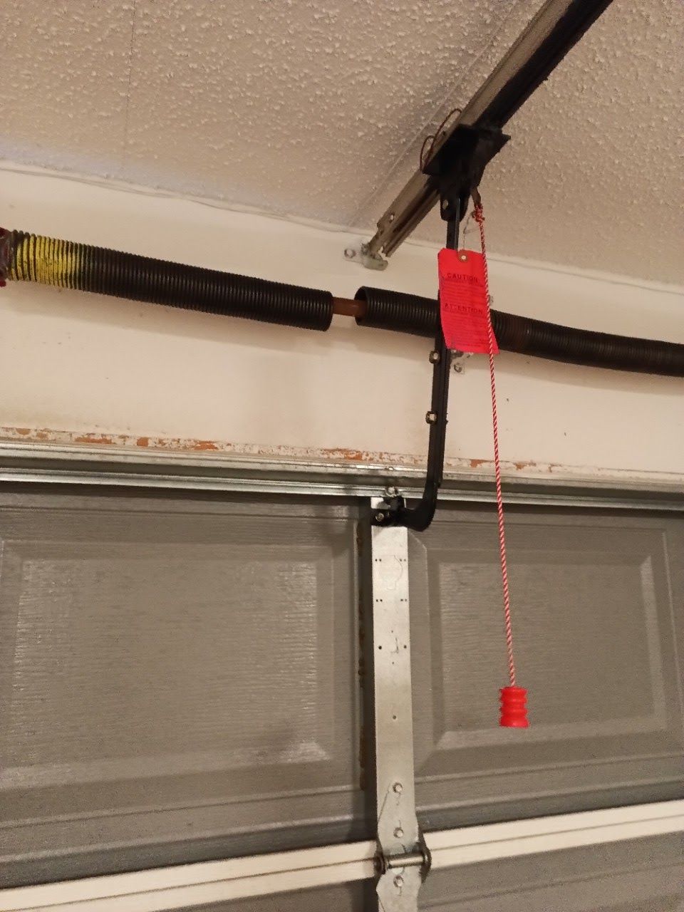 Garage door system with a black spring, track, and red safety tag hanging down.