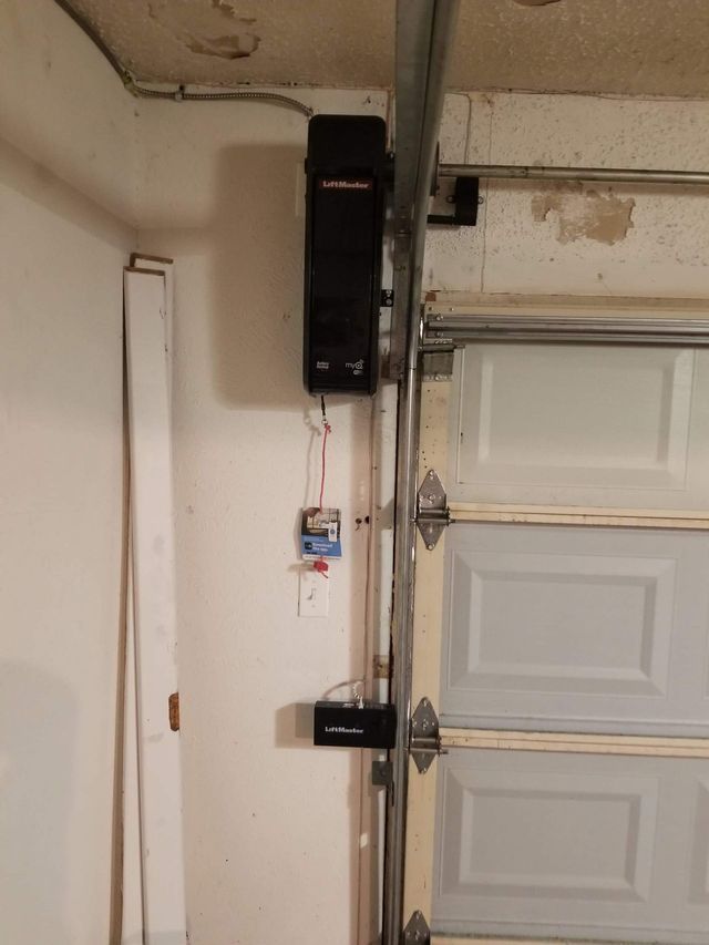 Garage door opener mechanism mounted on wall next to closed white garage door.