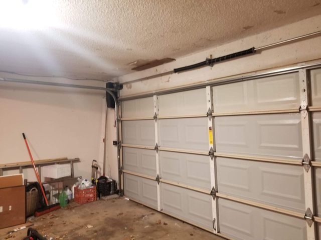 Garage interior with closed white panel garage door, tools, and a spring system.