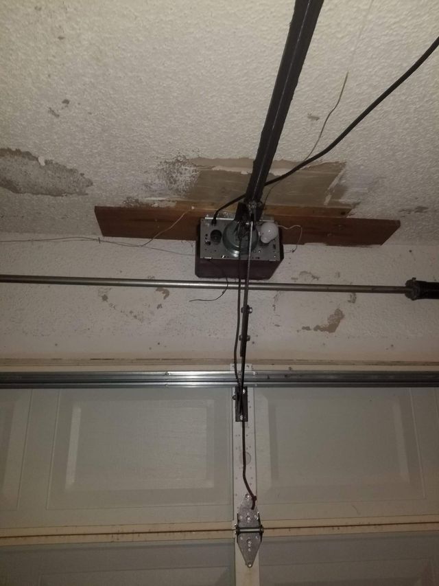 Garage door opener mounted on ceiling with power and control cables.