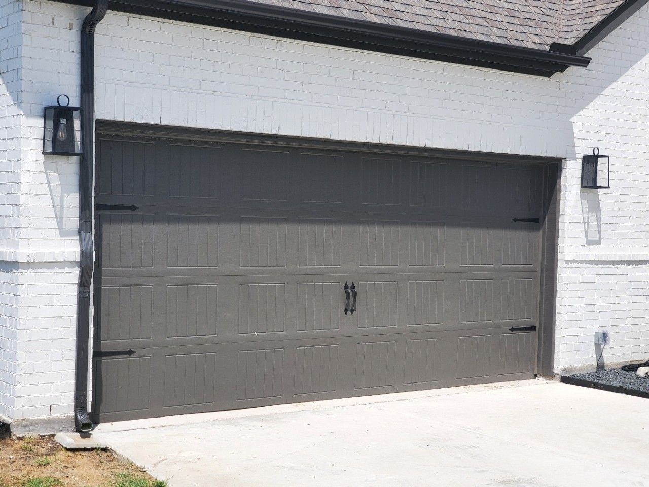 Gray garage door on a white brick house, flanked by black lights.