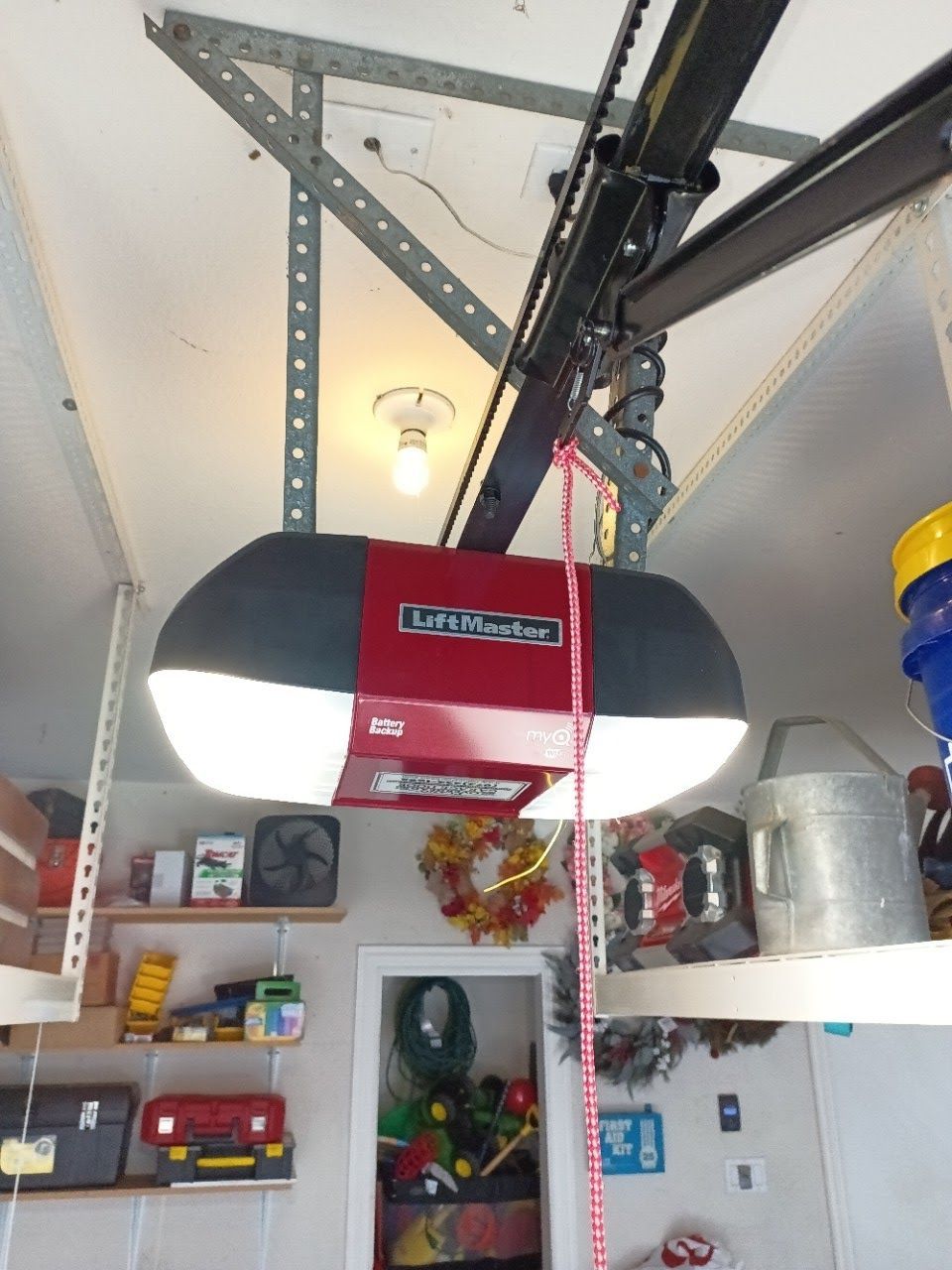 Garage door opener, red and black, with a chain, mounted on a garage ceiling.