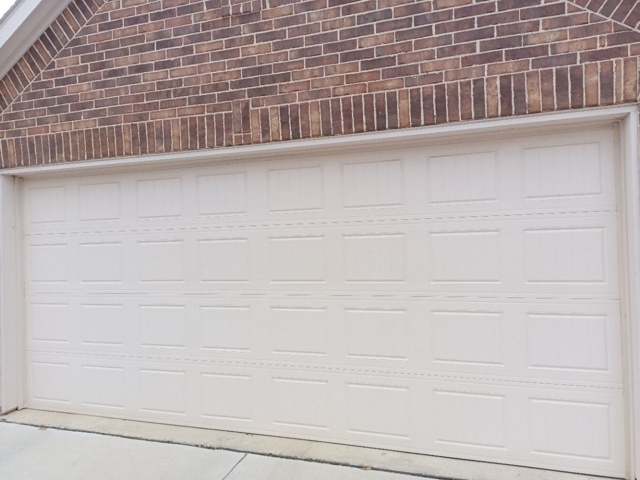 Beige garage door below a brick wall.