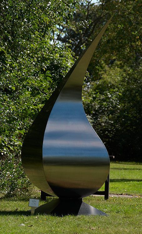 A large stainless steel sculpture is sitting in the grass in a park.
