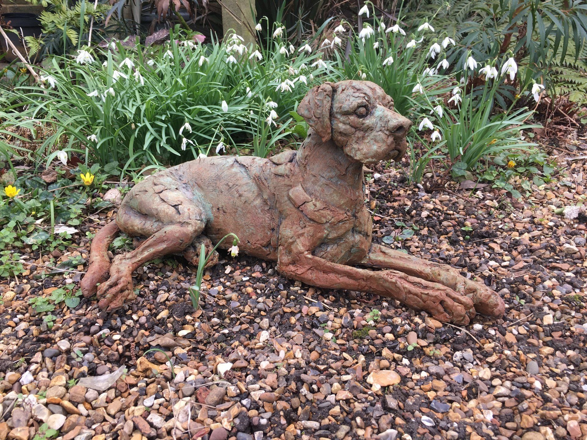 A statue of a dog laying on the ground in a garden.