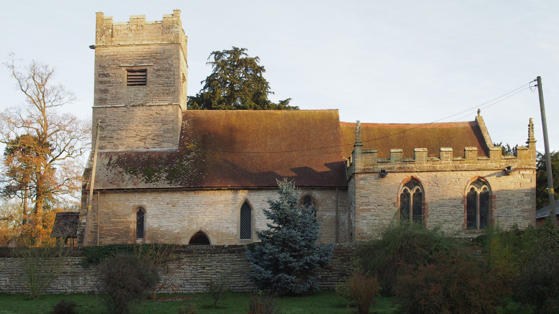 A large stone church with a brick tower is surrounded by trees and bushes.