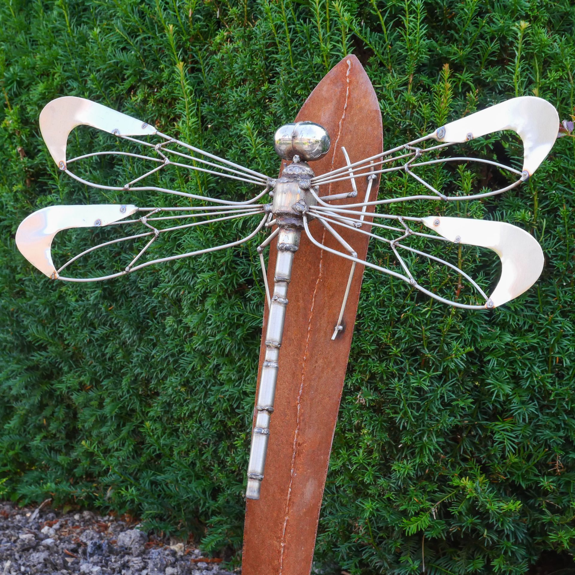 A metal dragonfly is sitting on a wooden stick