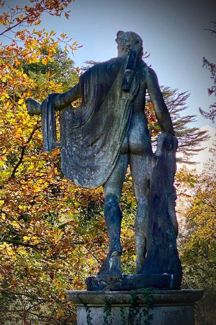 A statue of a man standing in Spetchley Park Garden with trees with golden leaves surrounding it