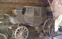 An old horse drawn carriage is sitting in a barn.