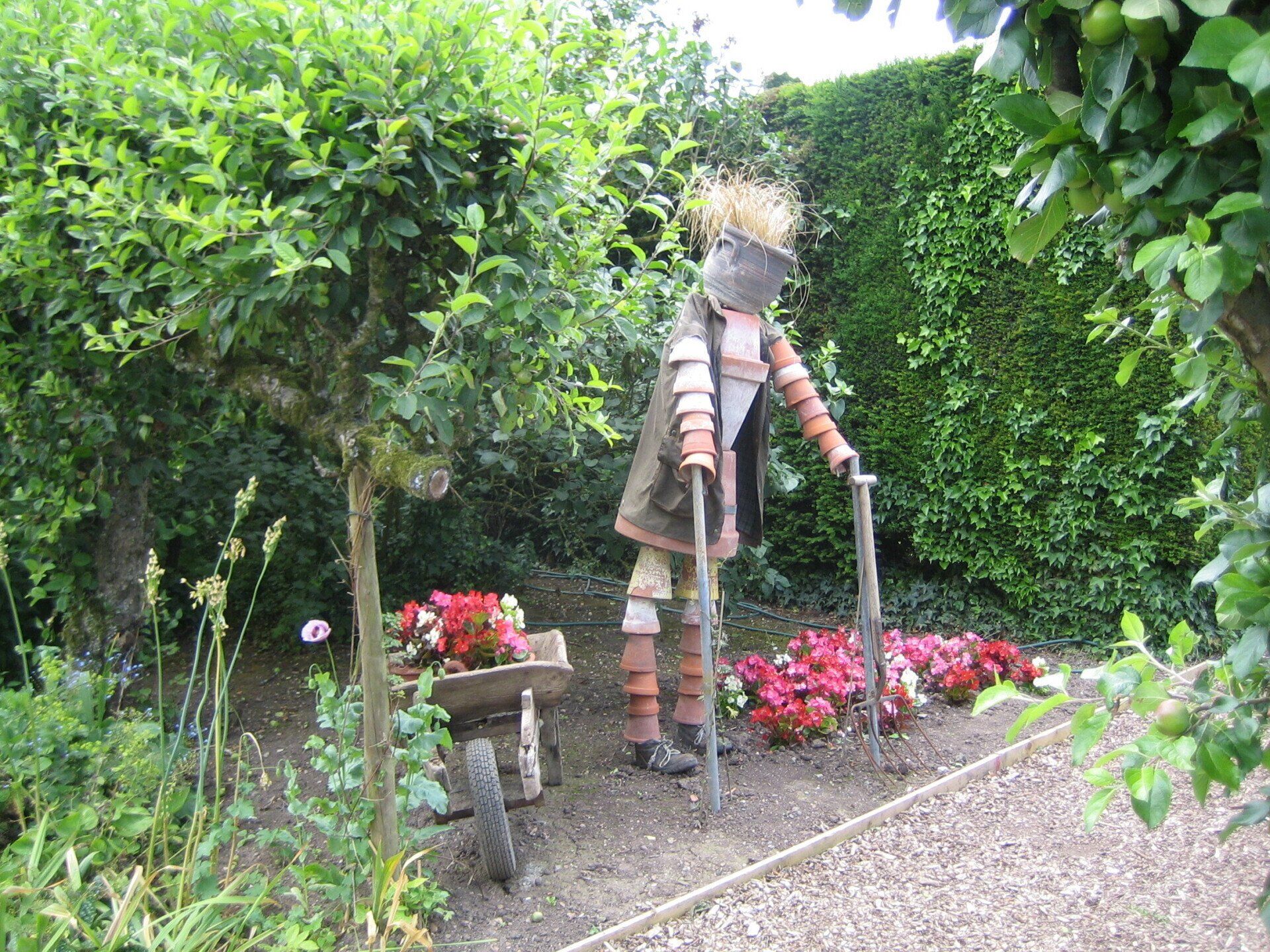 A scarecrow is standing next to a wheelbarrow in a garden.