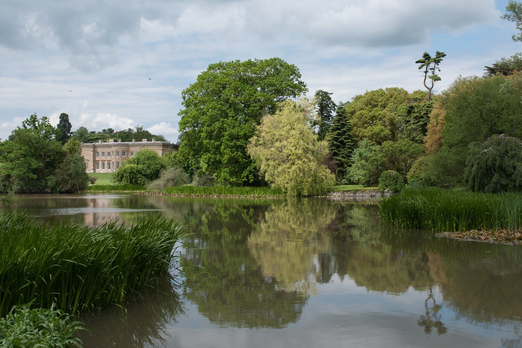 A large building is reflected in the water of a lake surrounded by trees.