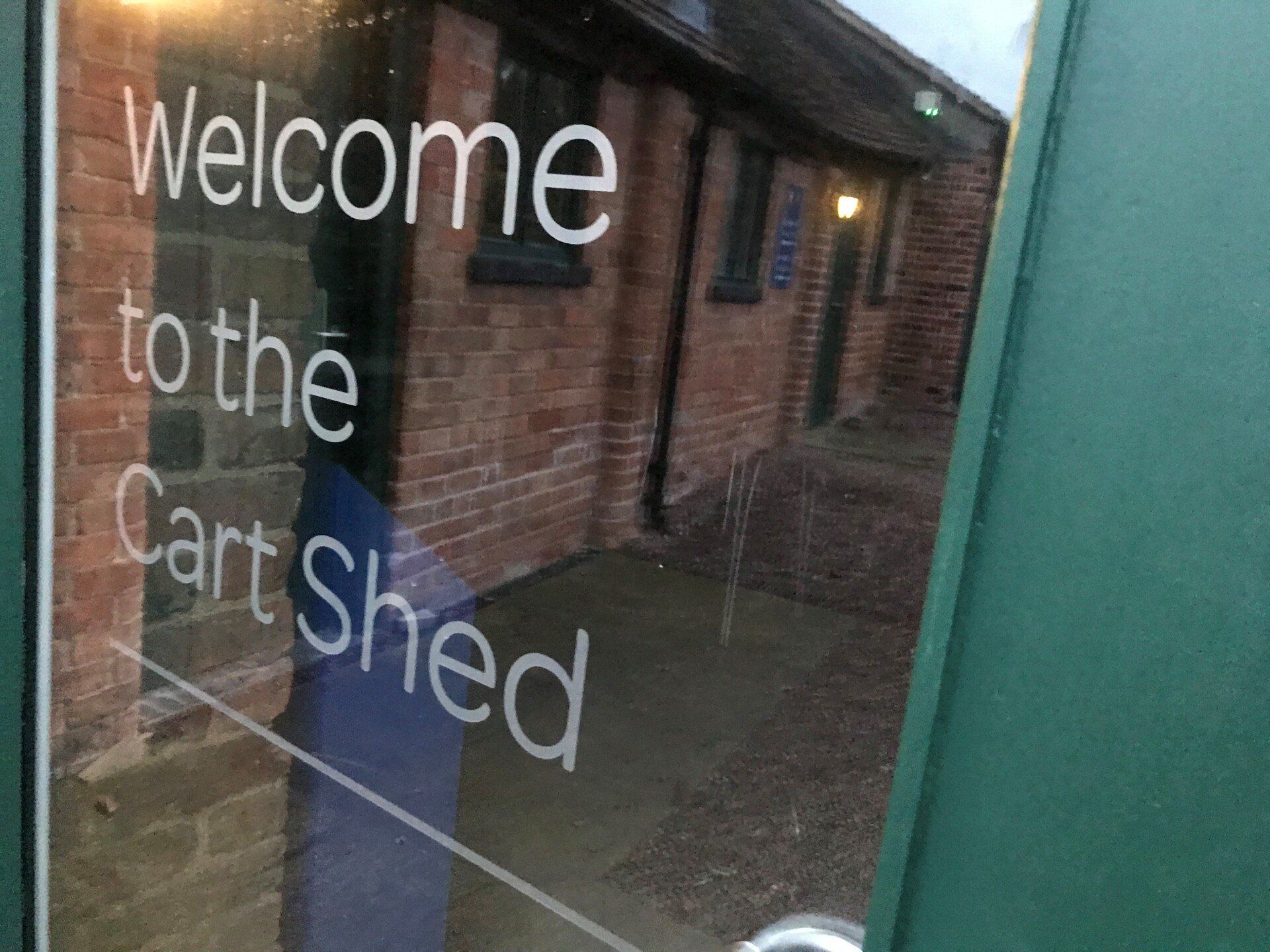A sign that says welcome to the cart shed is on a glass door.