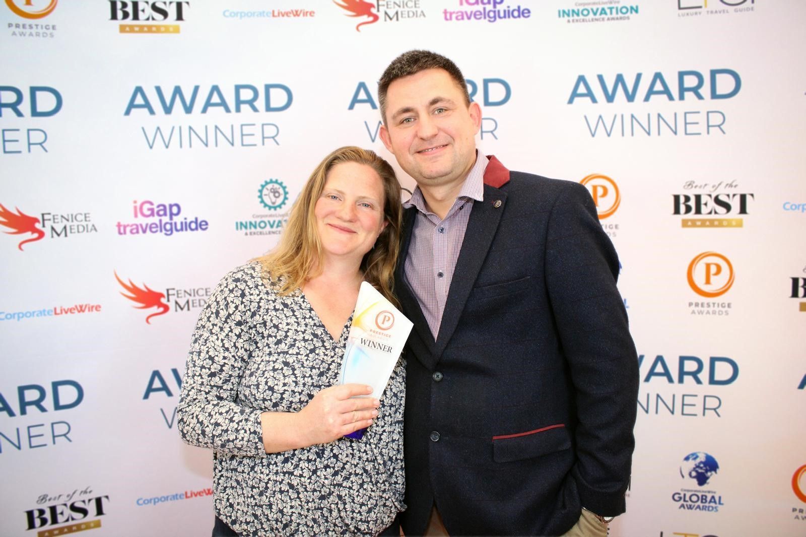 A man and a woman are posing for a picture in front of a wall that says award winner.